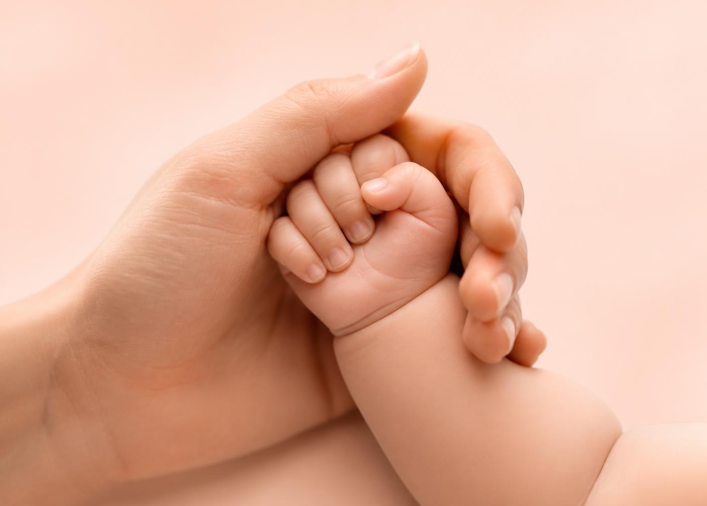 Mão adulta segurando com delicadeza a mão de um bebê.